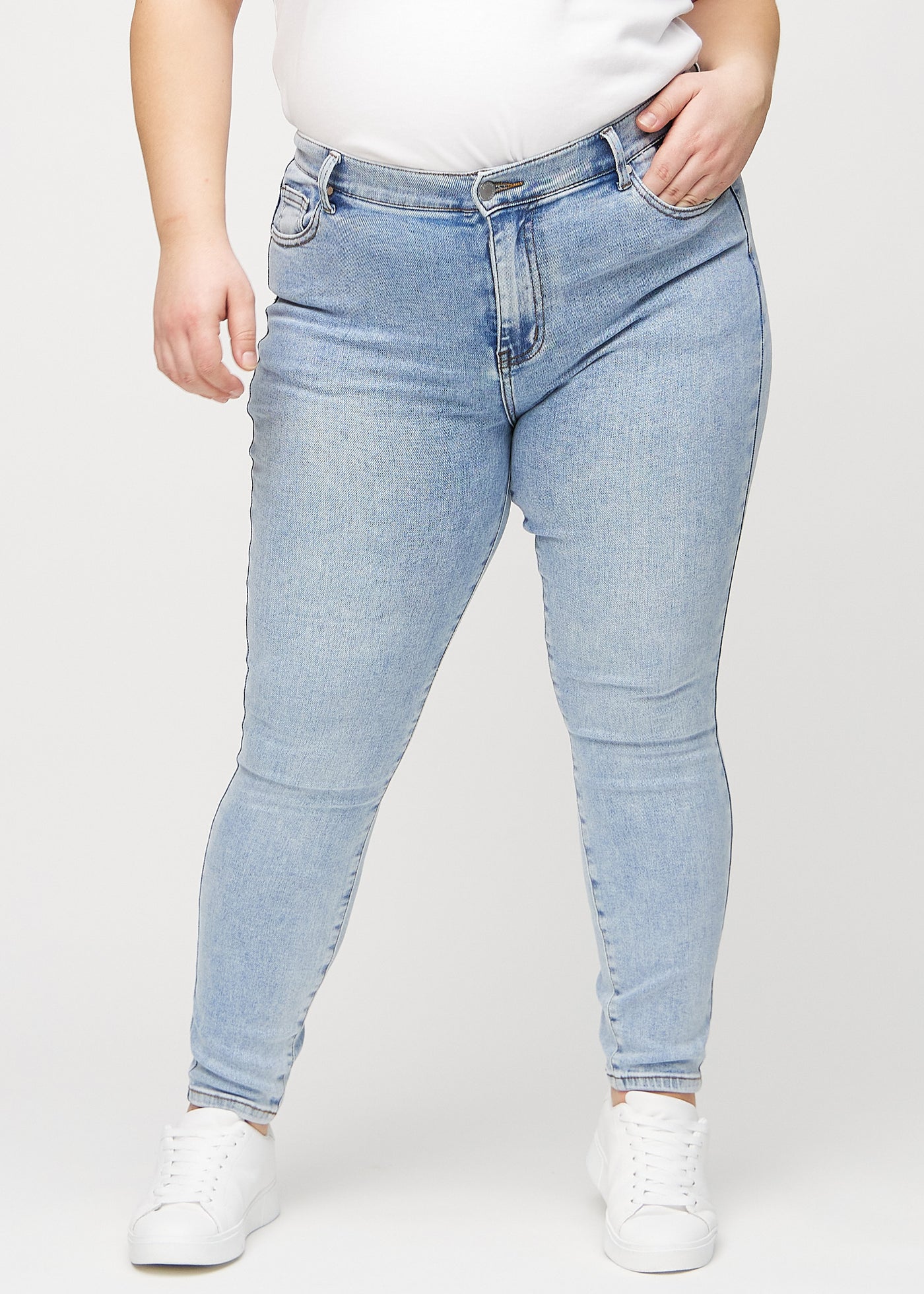 Lys denim skinny jeans, modelnavn Waves, som sidder tæt til benet på en plus-size model, set forfra.