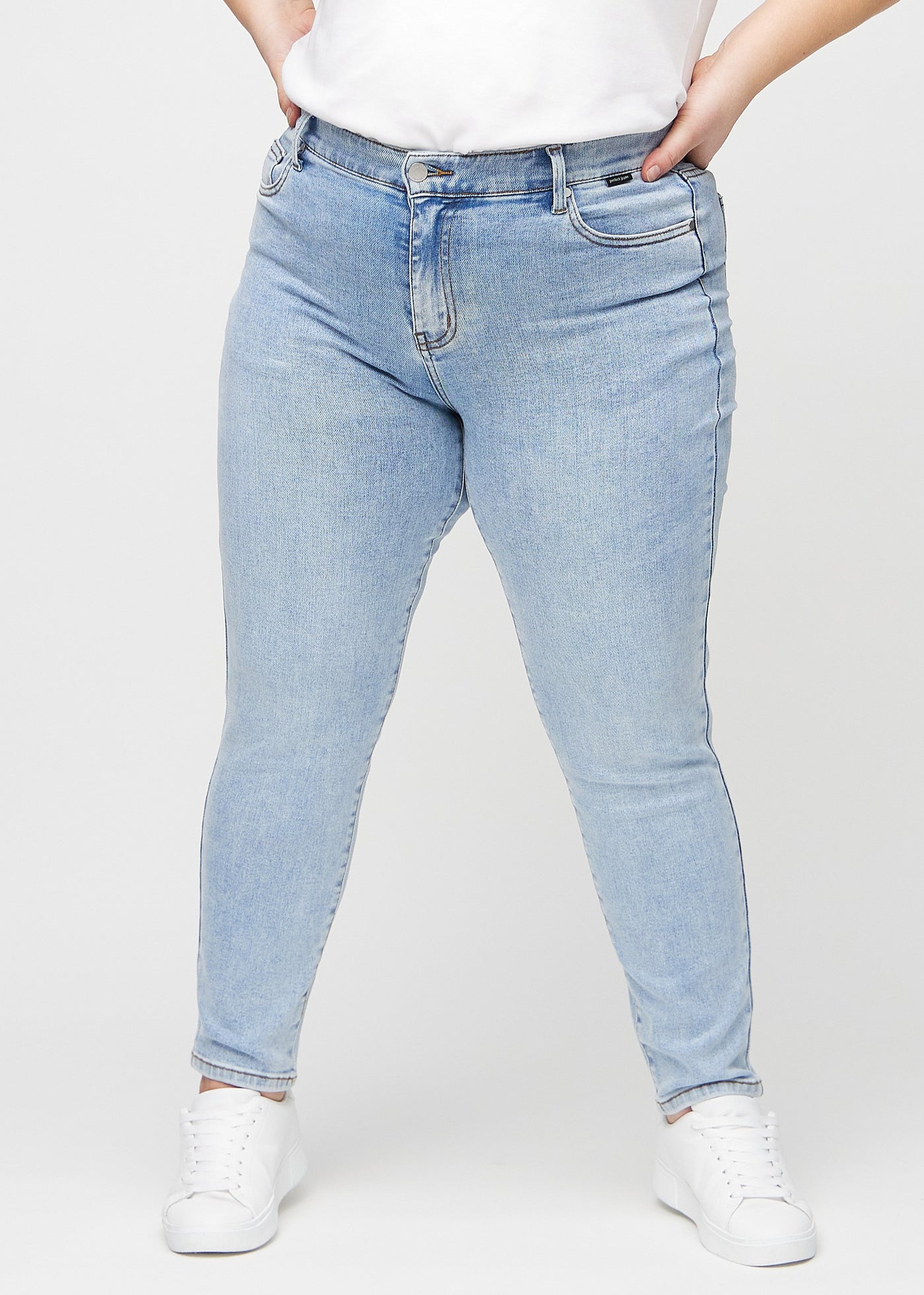 Lys denim slim jeans, modelnavn Waves, som sidder tæt til benet, dog lidt løsere ved anklen, på en plus-size model, set forfra.