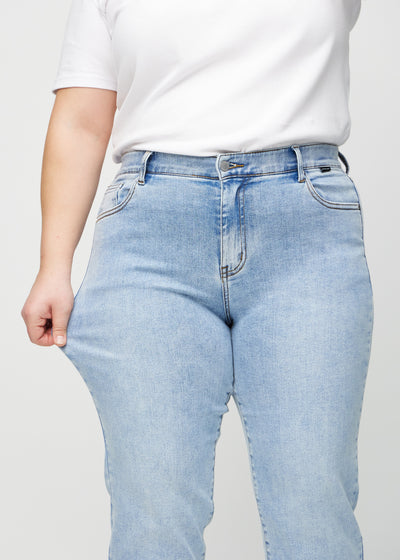 Plus-size model strækker jeansene ved låret for at vise stretch.